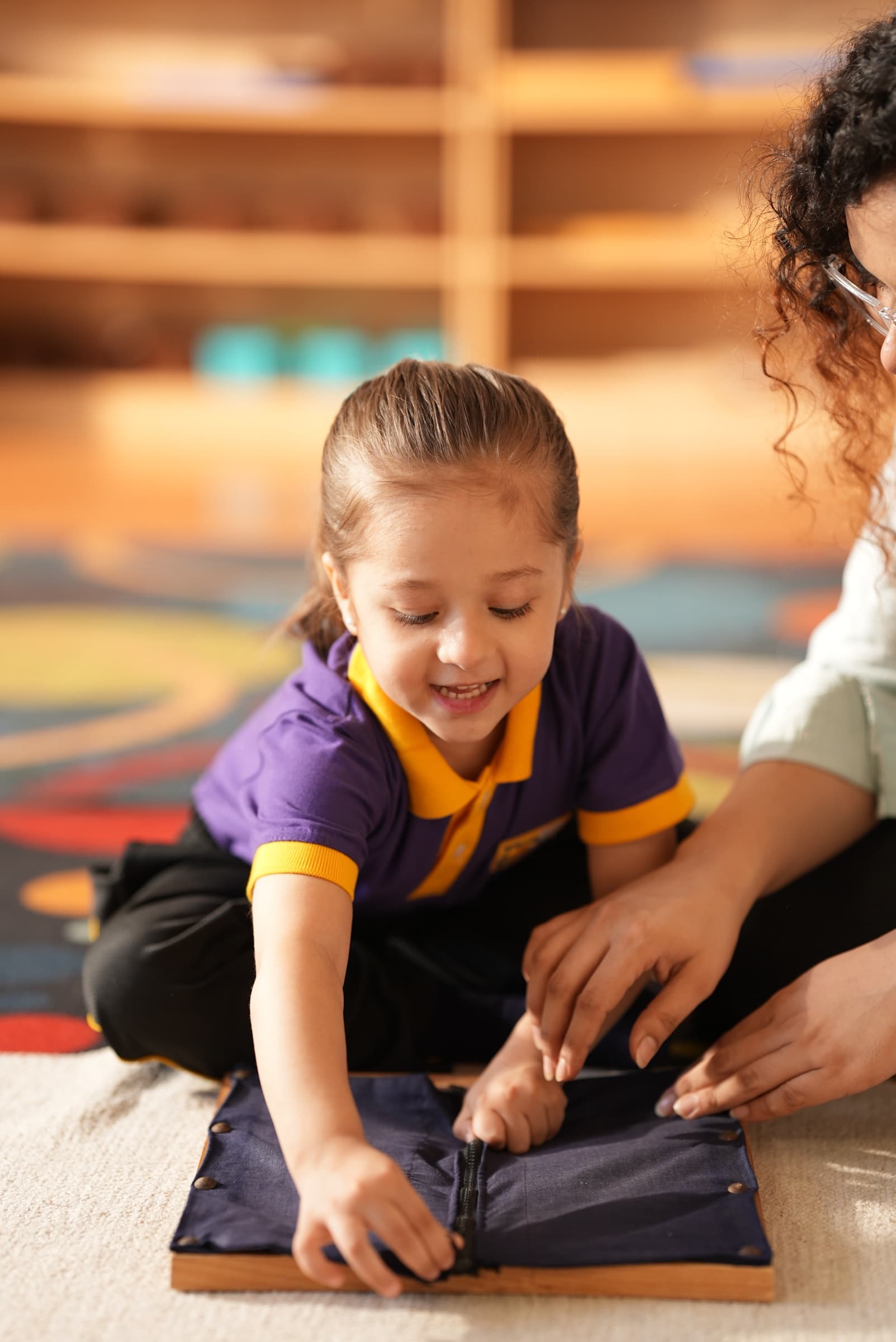 A child working a Montessori zipper frame with a teacher